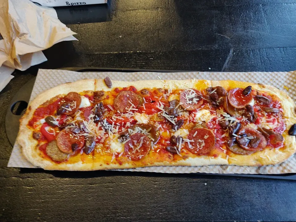 Pizza alargada con tomate y vegetales sobre tabla